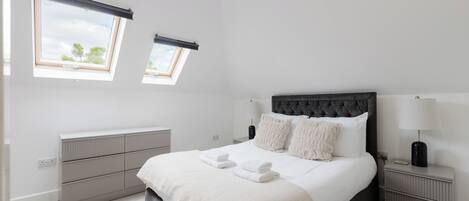A modern bedroom with a large bed, two bedside tables, a radiator, and a window with a view.