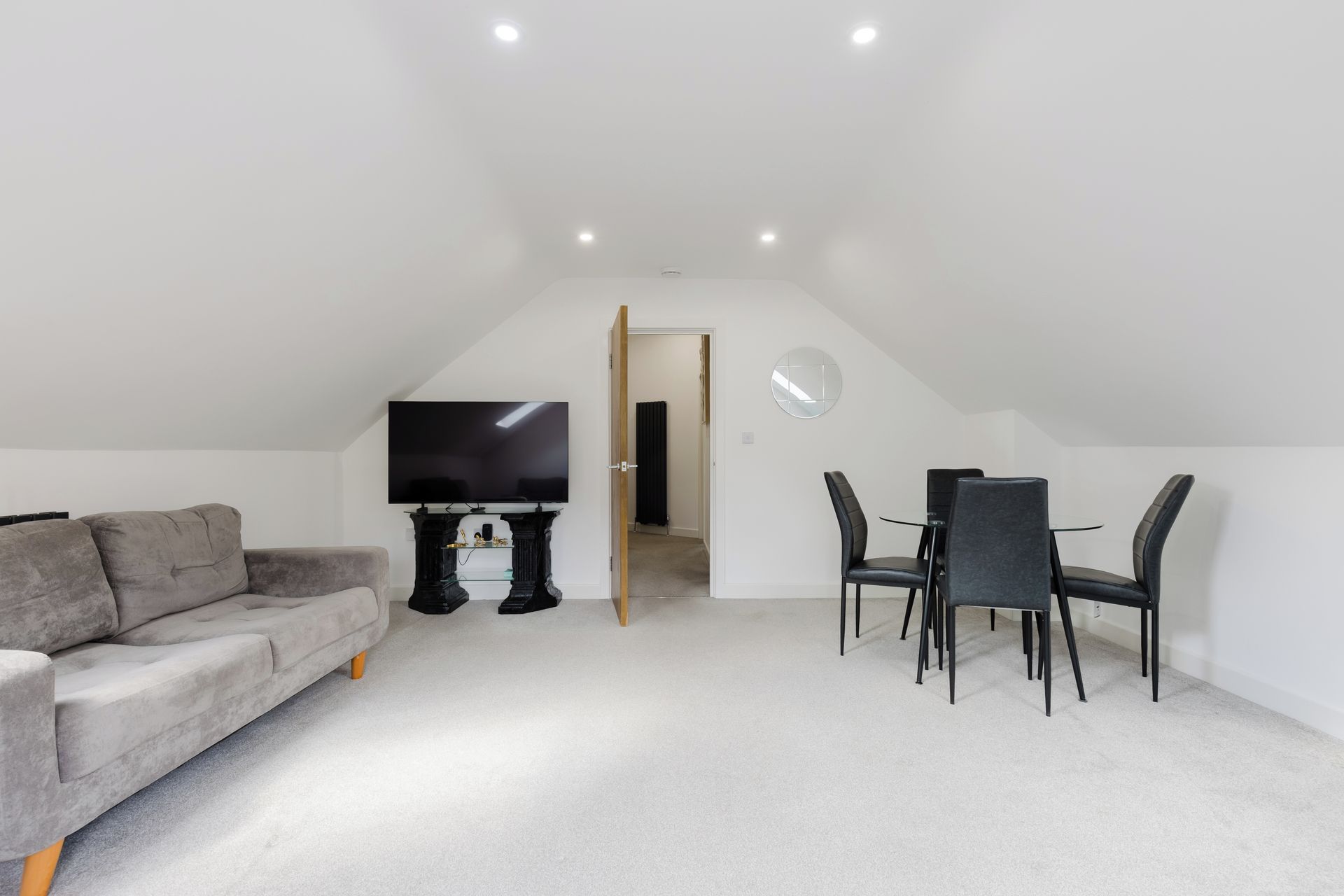 A modern living room with a flat-screen TV, a sofa, and a dining area with chairs.
