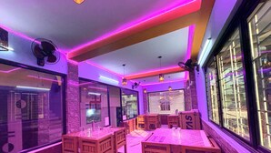 Ein Restaurant mit Holztischen und -stühlen, einem Ventilator und violetter Beleuchtung.