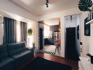 Ein modernes Wohnzimmer mit einer Couch, einem Essbereich mit Stühlen, einer Küche im Hintergrund und einer Treppe, die zu einer weiteren Ebene führt.