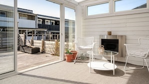 En moderne udendørs terrasse med glasdør, hvide fletstole, et lille bord og en pejs.