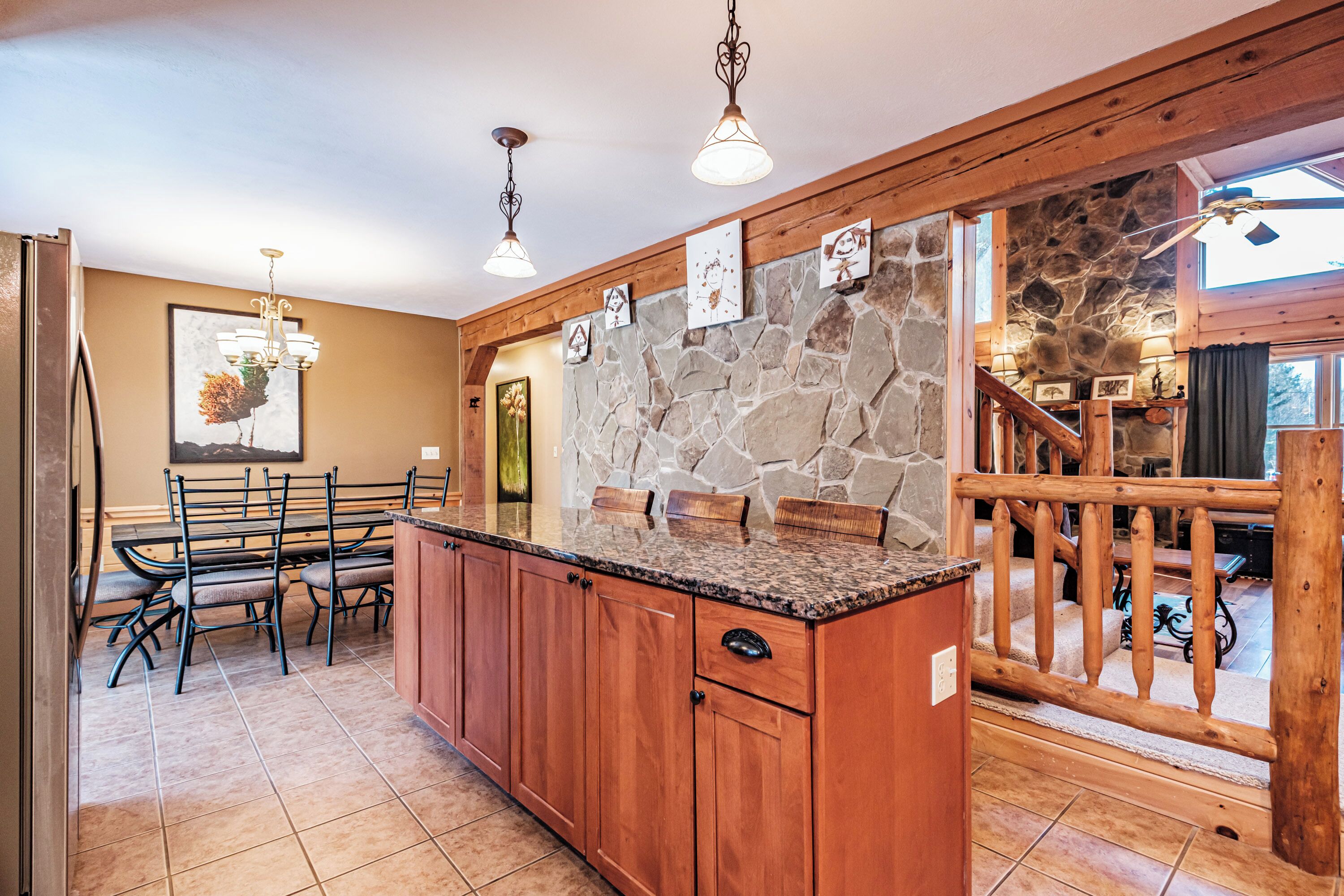 A kitchen with a stone wall, wooden cabinets, and a dining area with chairs.