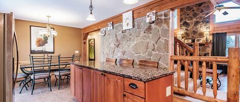 A kitchen with a stone wall, wooden cabinets, and a dining area with chairs.
