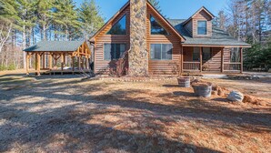 A log cabin with a stone chimney, large windows, and a porch. - Riverwood Chalet- Near Sunday River (Newry)