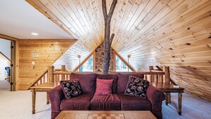 A cozy room with a wooden ceiling, a couch with floral cushions, and a chess table. - Riverwood Chalet- Near Sunday River (Newry)