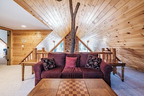 A cozy room with a wooden ceiling, a couch with floral cushions, and a chess table.