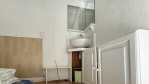 Habitación pequeña con cama, una mesita, un lavamanos blanco y un armario.