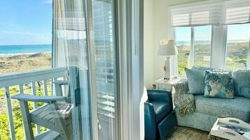 Un balcon avec vue sur la plage, un canapé avec des coussins, une lampe et un pouf en osier.