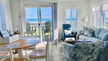 Une pièce avec vue sur l’océan, un ventilateur de plafond, un fauteuil bleu, une table à manger en bois et un canapé à motifs bleus et blancs.