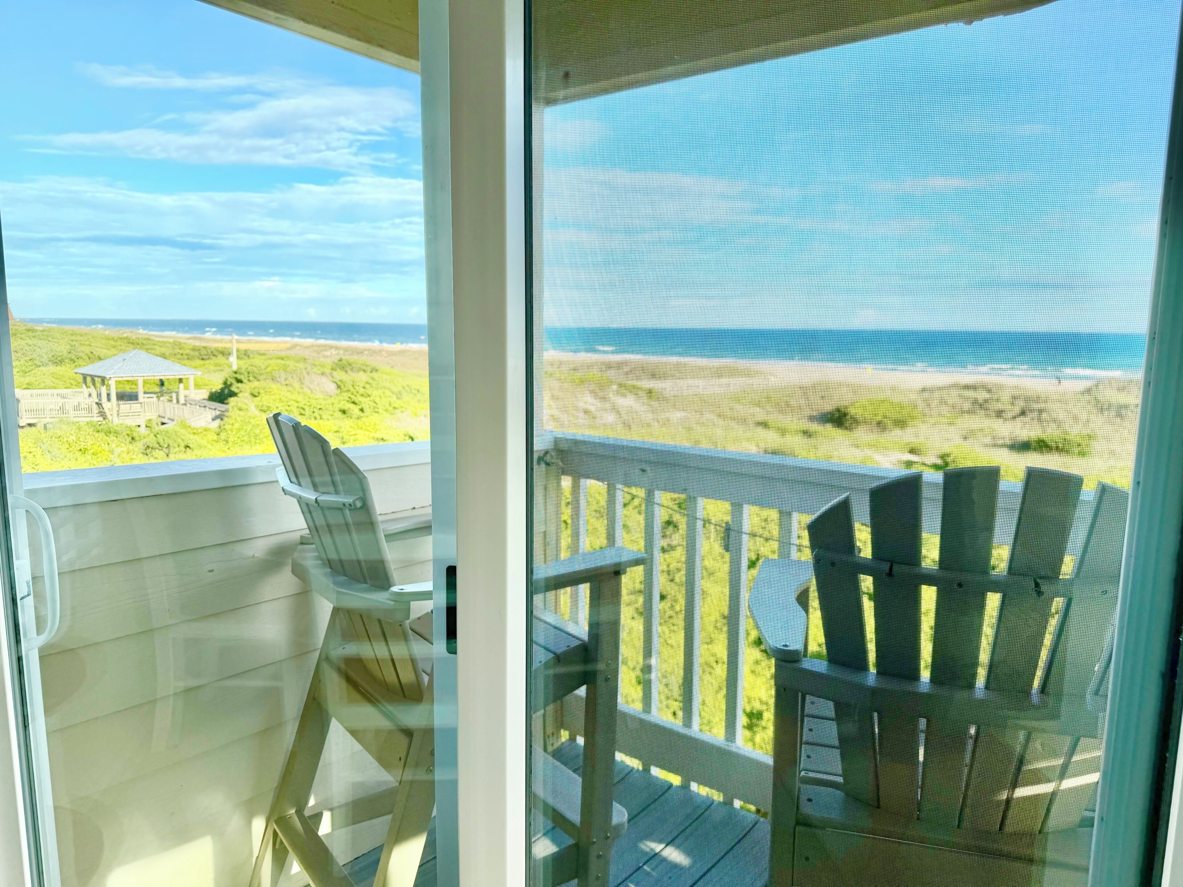 Ein Balkon mit Blick auf den Strand, eine kleine Struktur und zwei Adirondack-Stühle.