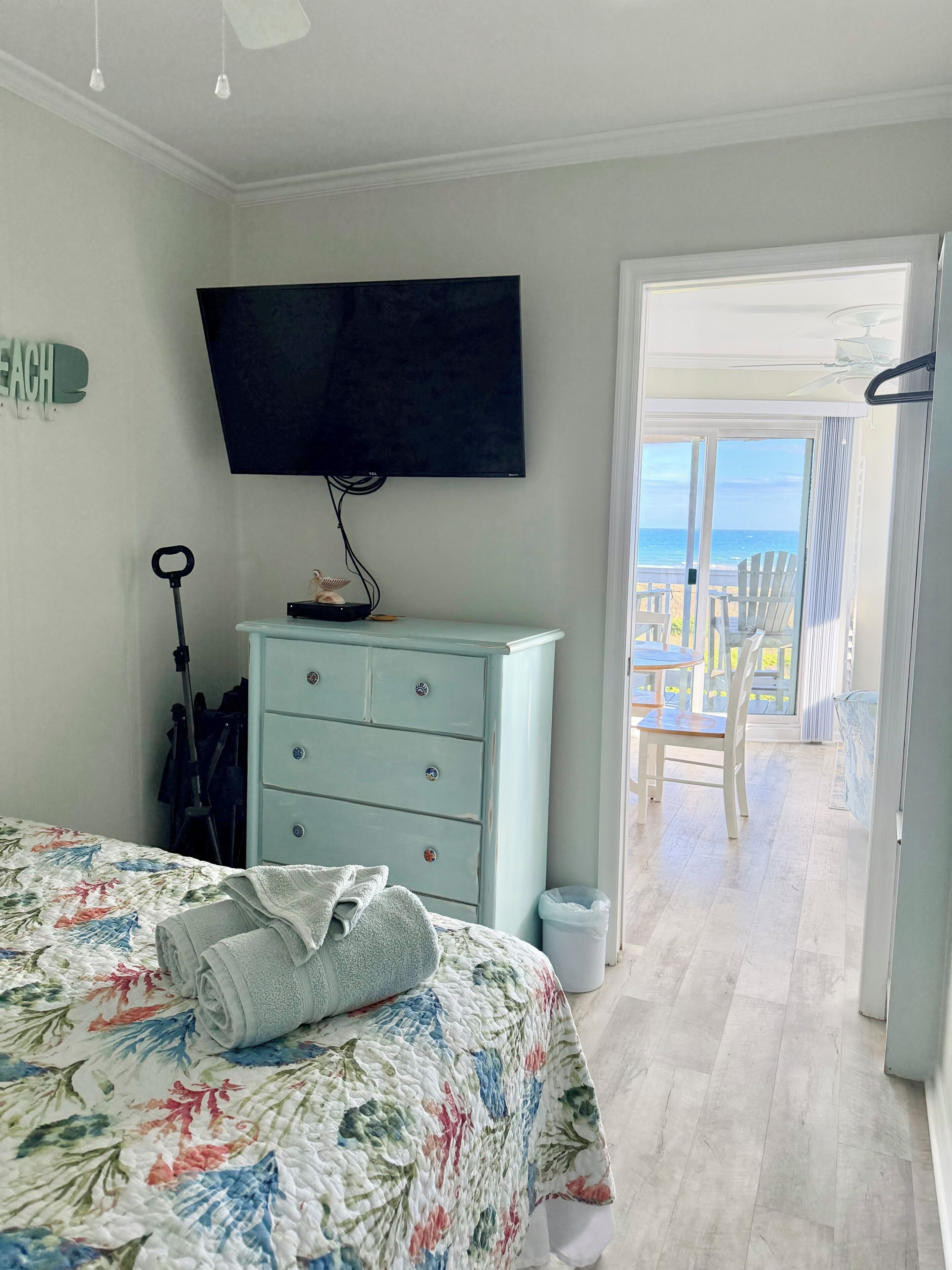 Un dormitori amb un llit, una petarrera, una televisió i vista a la platja per una porta oberta.