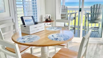 Un coin repas avec une table ronde, des chaises blanches et une vue sur la plage.