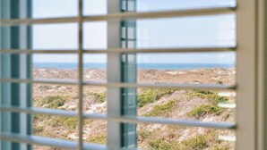 A view through a window with a grid pattern, featuring a landscape with sparse vegetation and a distant horizon. - Seaside Retreat - oceanfront, pool sleeps 4, views, previous”Leg-a-Sea” (Atlantic Beach)