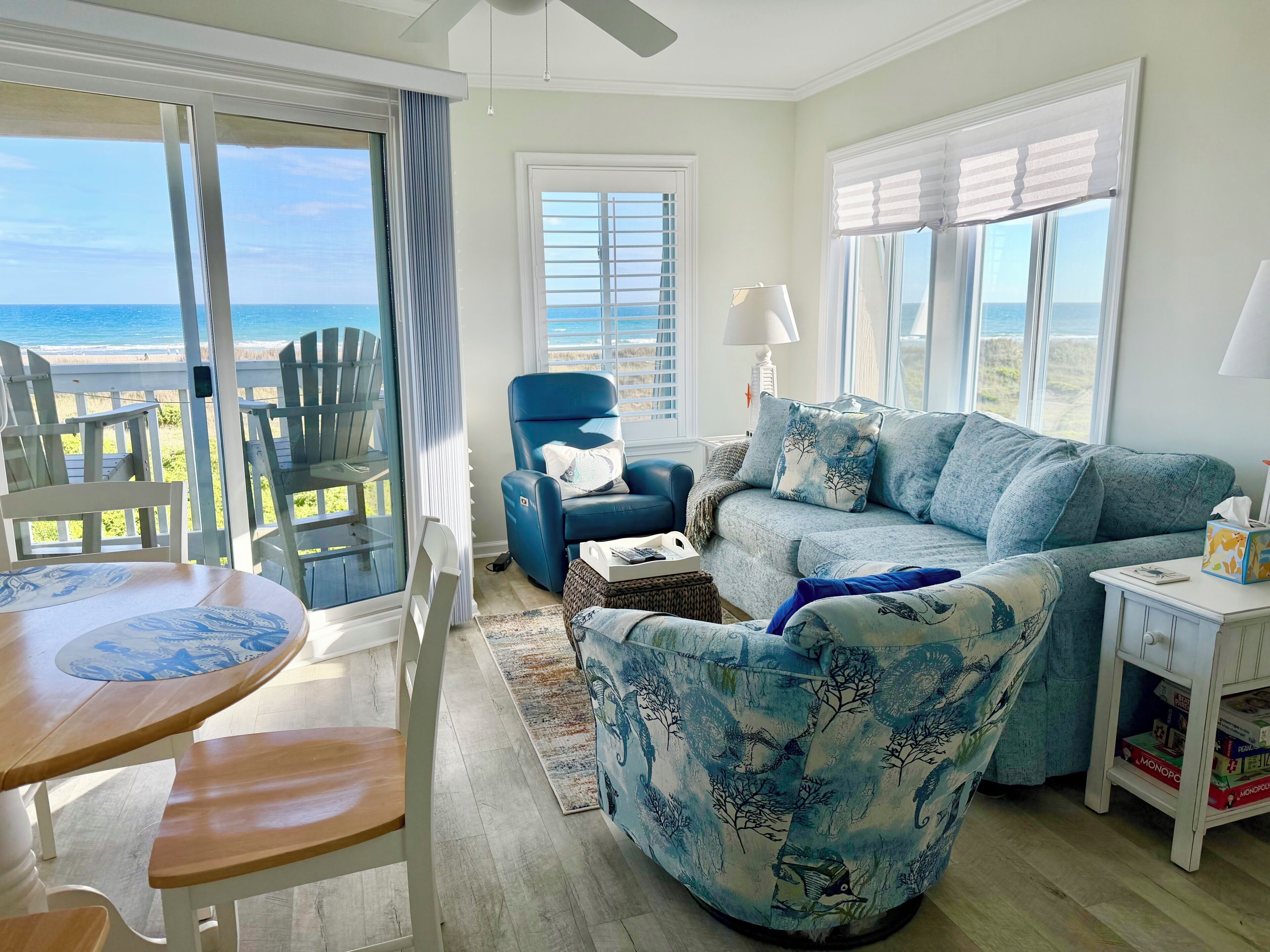 Una sala de estar con vista al océano, un sillón azul, un sofá, una mesa y una estantería.