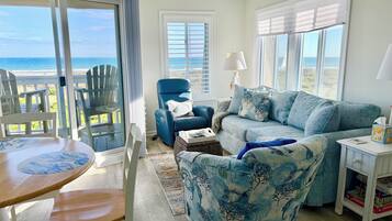 Una sala de estar con vista al océano, un sillón azul, un sofá, una mesa y una estantería.