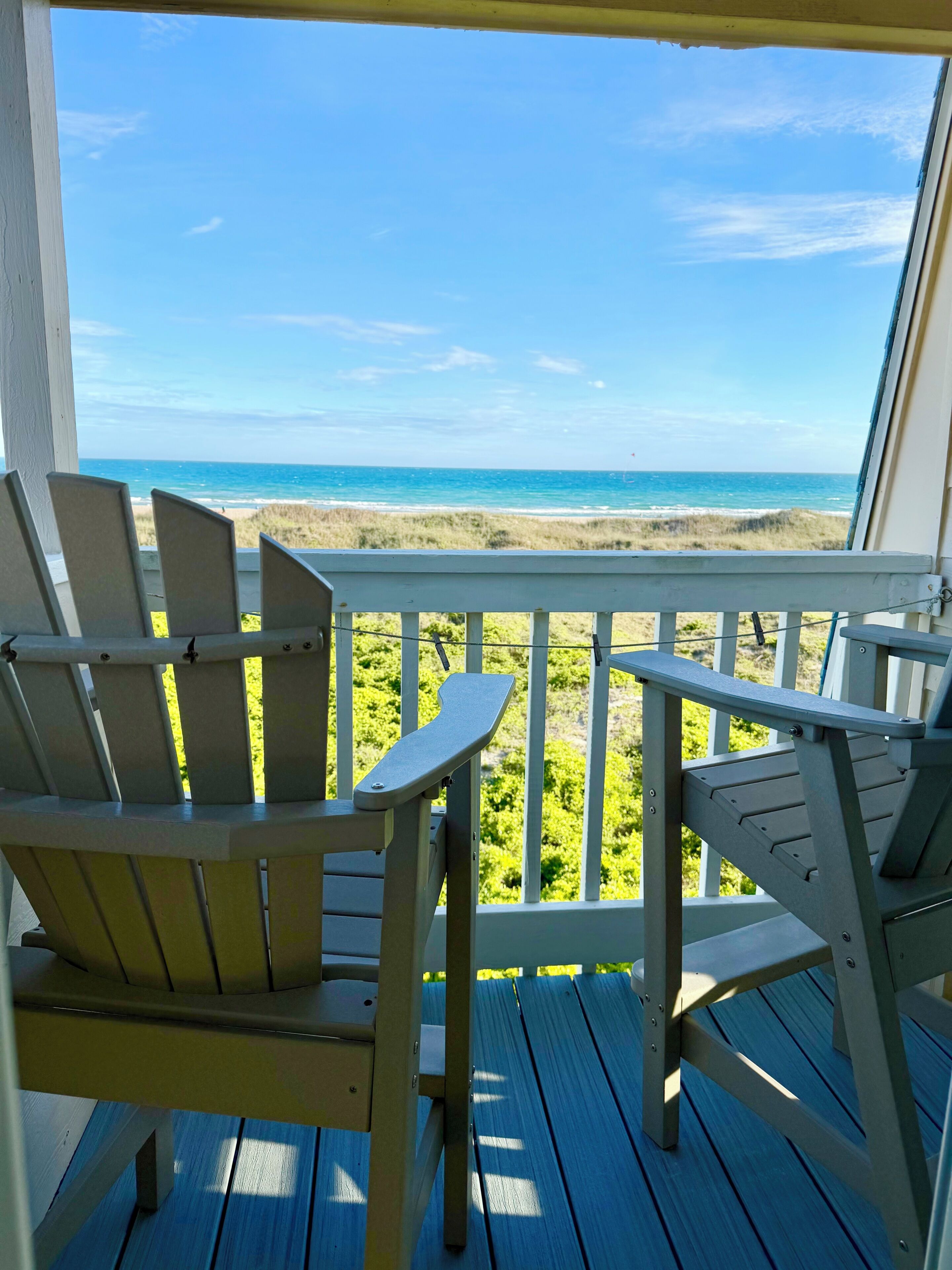 A wooden deck with two Adirondack chairs facing a beach view.