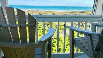 A wooden deck with two Adirondack chairs facing a beach view.