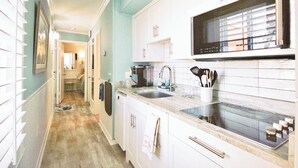 A narrow hallway leading to a kitchen with white cabinets, a microwave, and a sink. - Seaside Retreat - oceanfront, pool sleeps 4, views, previous”Leg-a-Sea” (Atlantic Beach)