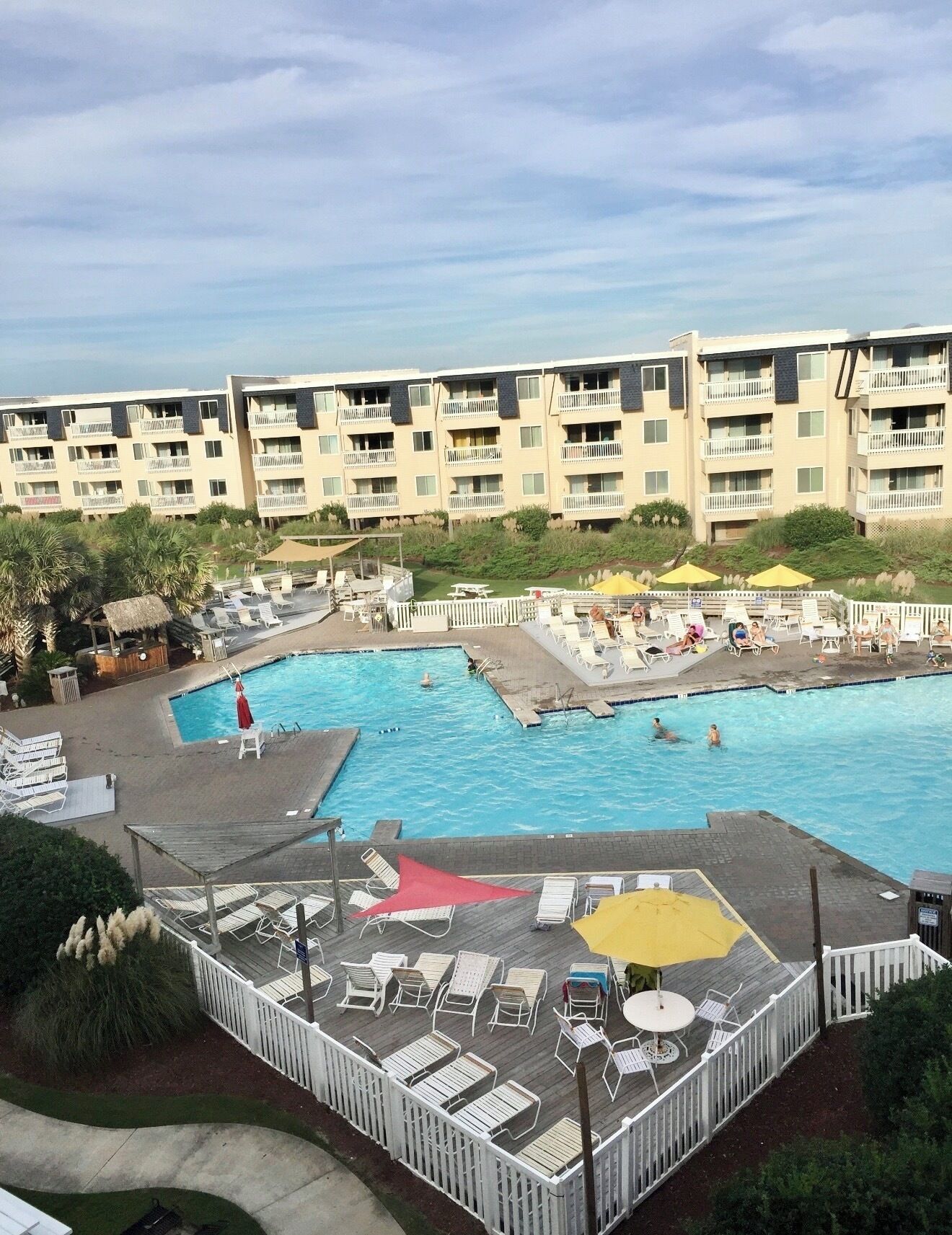 A hotel with a large swimming pool, multiple balconies, and outdoor seating areas.