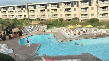 A hotel with a large swimming pool, multiple balconies, and outdoor seating areas.