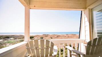 Un balcó amb dues cadires Adirondack blanques, un sostre de fusta i vista a la platja.