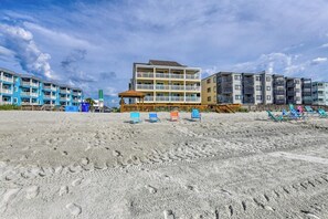 Ein Strandhotel mit mehreren Balkonen, Liegestühlen und einem Sandstrand.