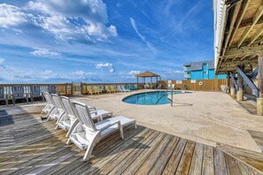 A pool area with lounge chairs, a wooden deck, and a building with a blue exterior. - Afterdeck 105 - Two Bedroom, Two Bath Oceanfront Condo (Garden City Beach)