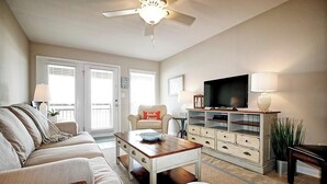 Een woonkamer met een bank, salontafel, tv-meubel en een plafondventilator.