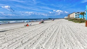 Een strand met een pier, zandstrand en gebouwen met balkons.