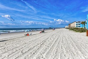 Ein Strand mit einem Steg, Sandstrand und Gebäuden mit Balkonen.