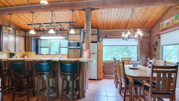 Una cocina rústica con armarios de madera, una zona de bar con taburetes, una mesa de comedor con sillas y un ventanal que proporciona luz natural.