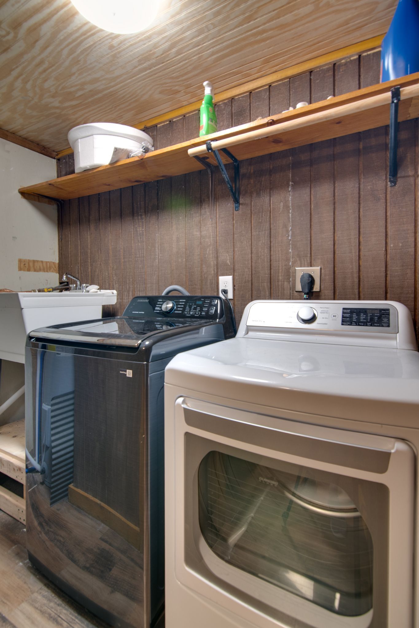 A laundry area with two washers and dryers, wooden shelves above, and a wooden wall.