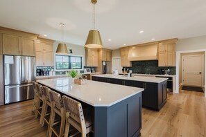 Eine moderne Küche mit Holzschränken, Edelstahlgeräten und einer großen Kochinsel mit Sitzgelegenheiten.