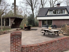 Une cabane en bois avec un toit en pente, un mur en briques et un espace patio comprenant une table et des chaises.