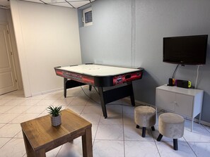 Une pièce avec un baby-foot, une télévision, un meuble et une petite table sur laquelle est posée une plante.