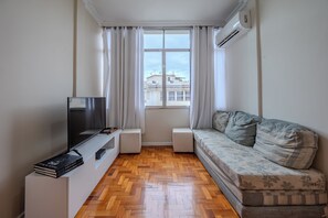 Uma sala de estar moderna com sofá, televisão, janela com cortinas e piso de madeira em padrão herringbone.