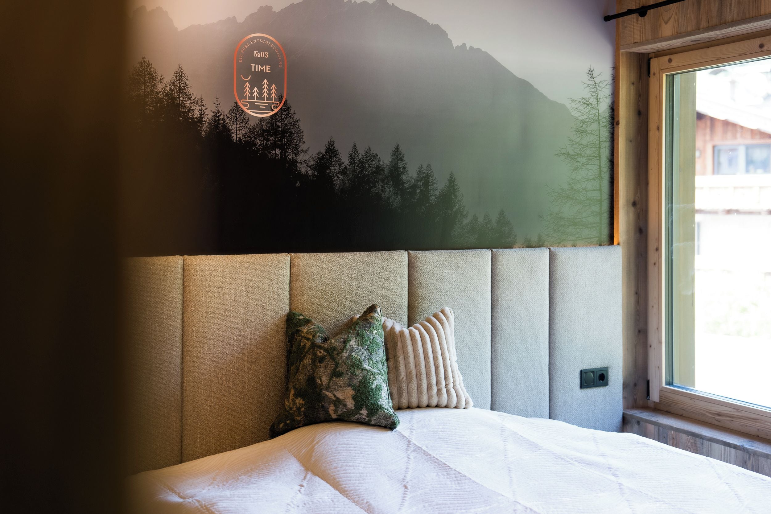 Un dormitorio con cama, cabecera, ventana y pared con un mural de temática natural.
