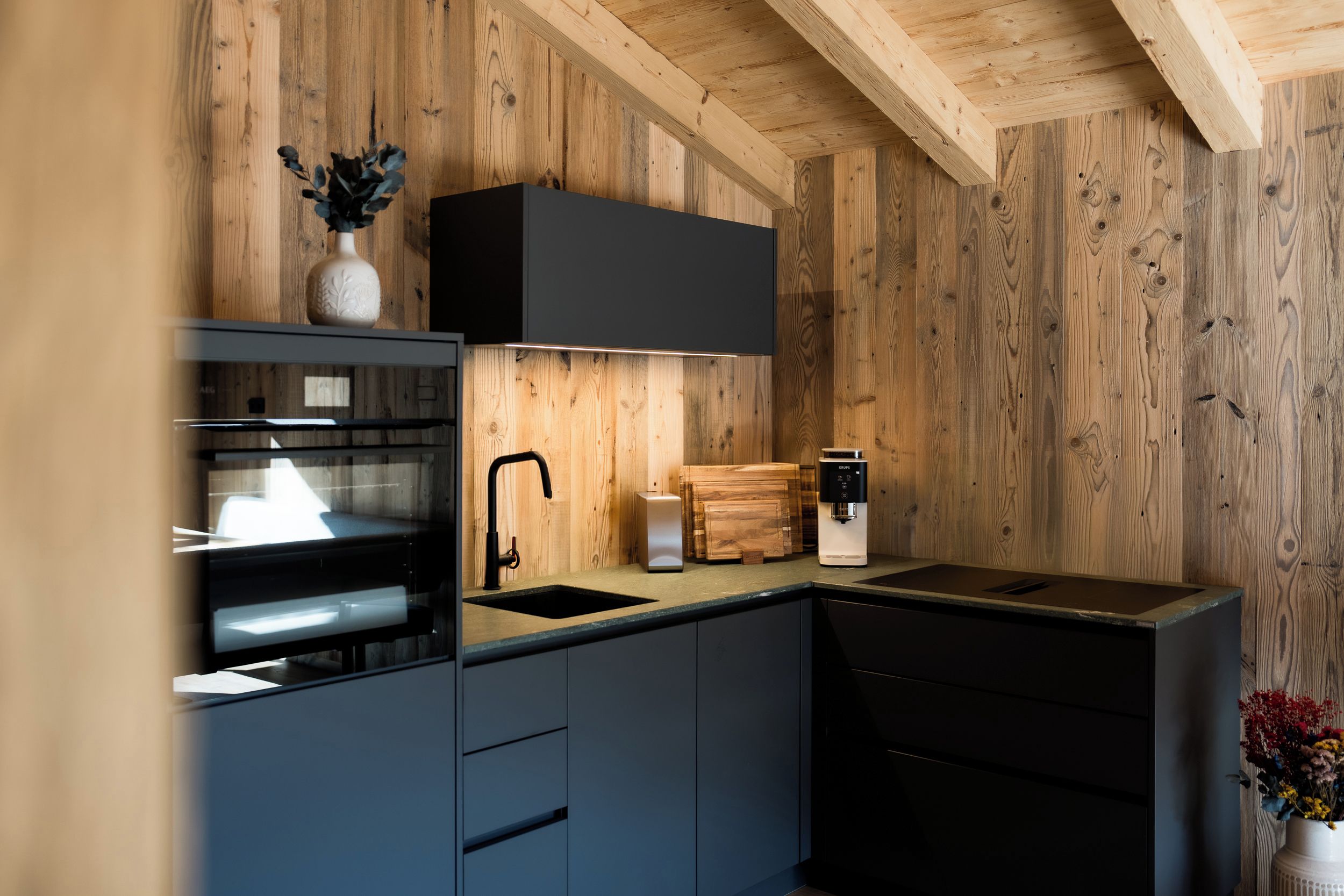 A modern kitchen with wooden walls, a black countertop, and a built-in oven.