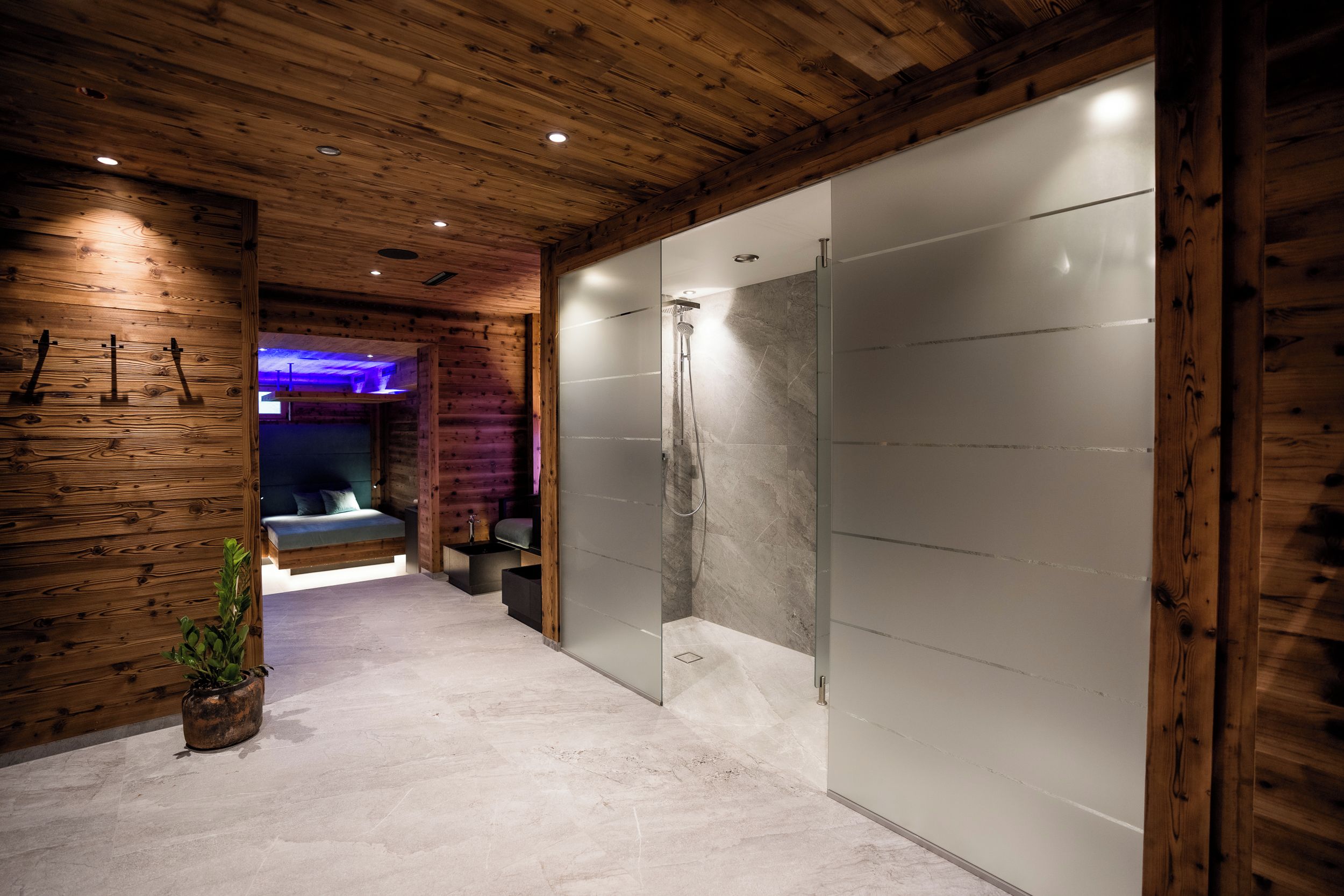 A modern bathroom with a wooden ceiling, a glass shower enclosure, and a bed with a blue headboard.