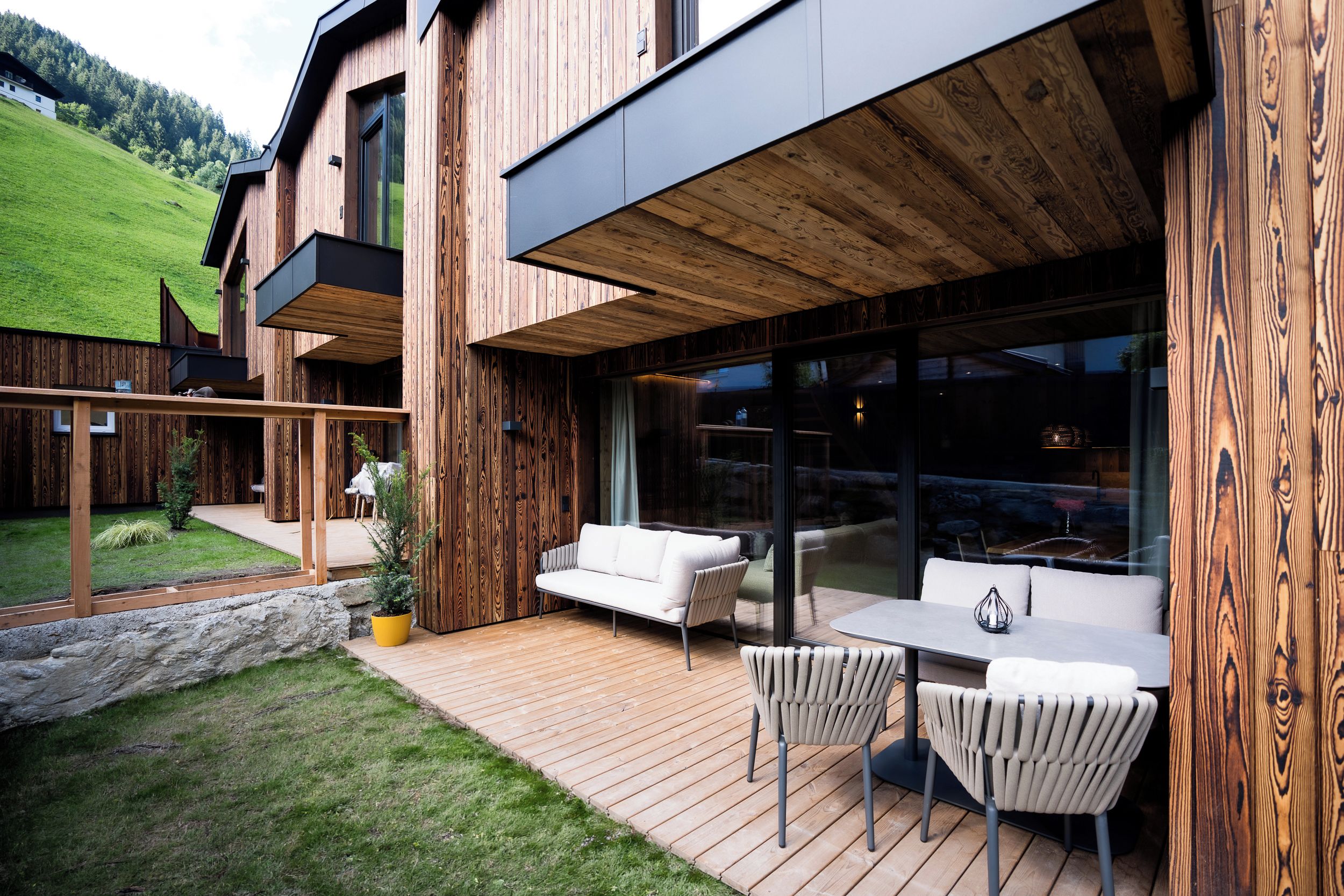 Una casa de madera moderna con un patio que cuenta con un sofá, sillas y una mesa.
