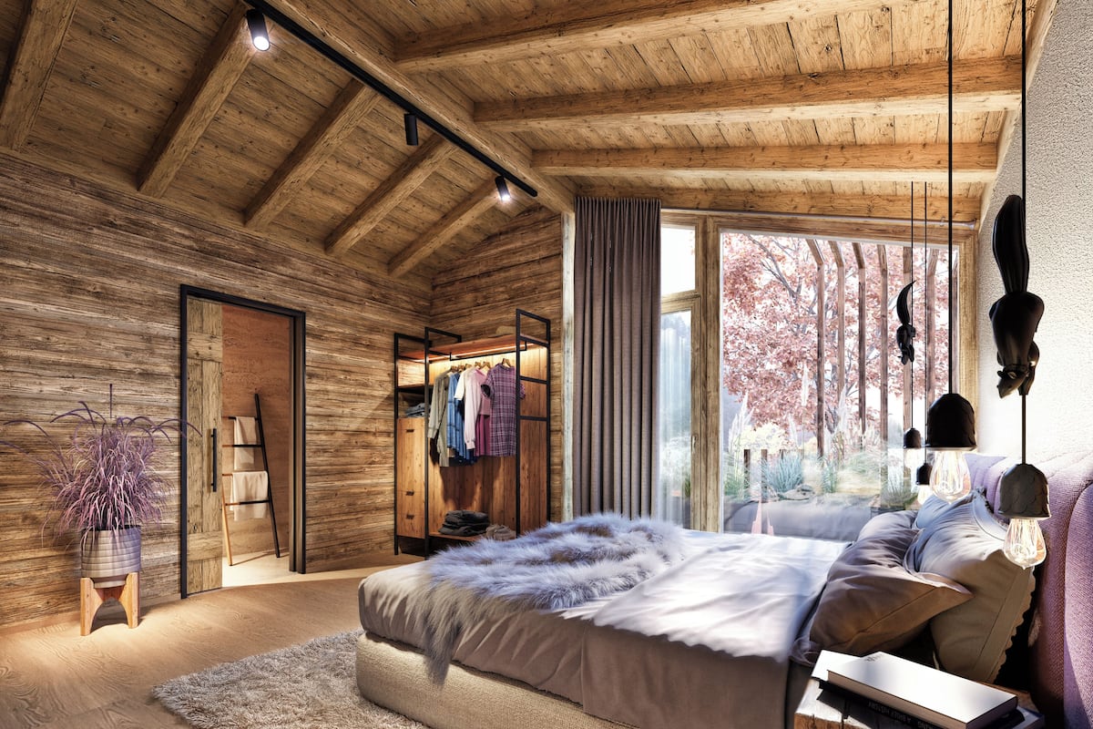 Ein Schlafzimmer mit Holzbalkendecke, einem Bett mit flauschiger Decke, einem Nachttisch mit Lampe und einem Fenster mit Blick auf Bäume.