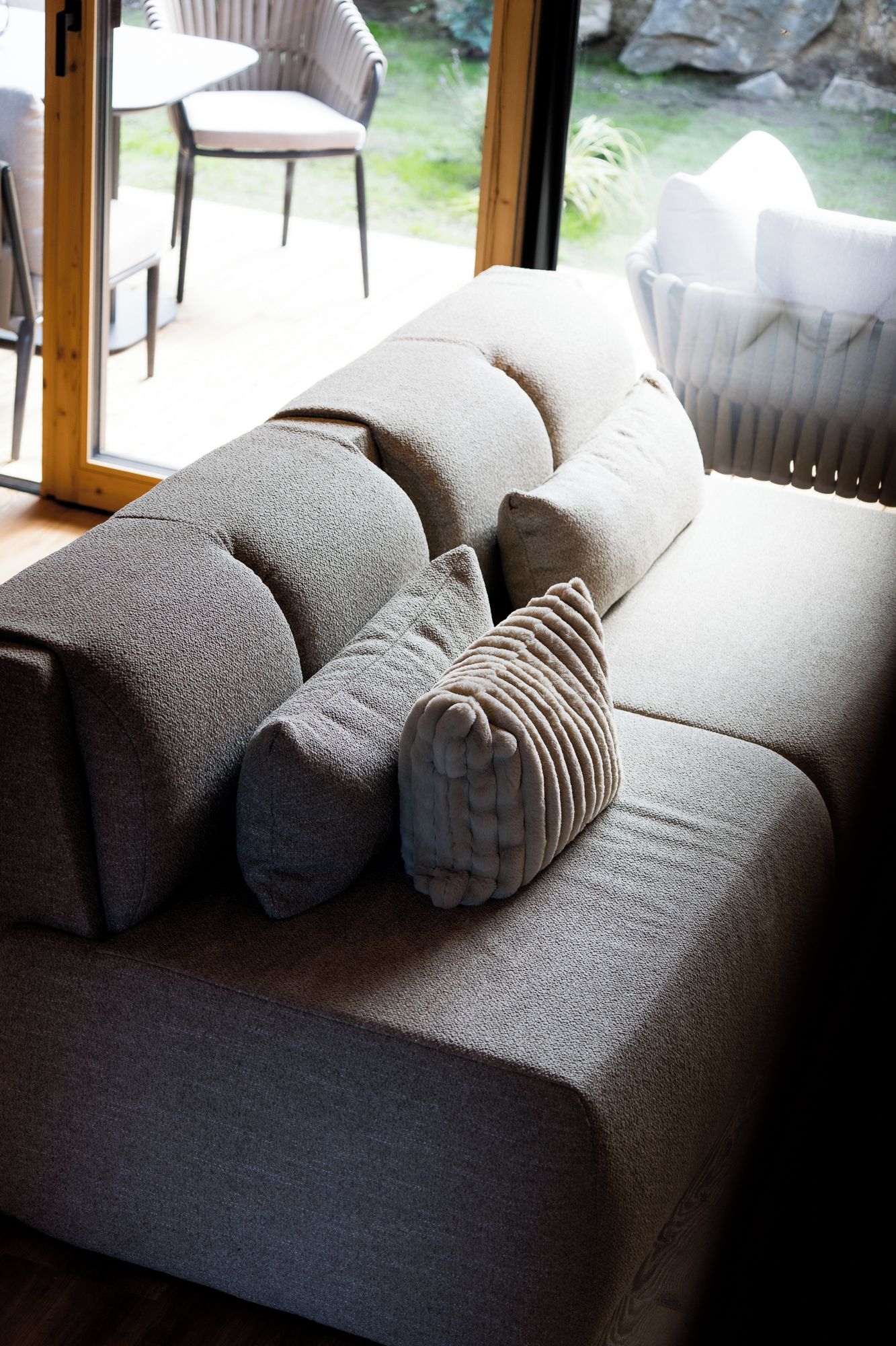 Una sala de estar moderna con un sofá grande gris, un cojín estampado y vistas al exterior a través de un ventanal.