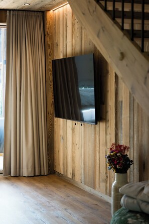 A room with a wooden wall, a flat-screen TV mounted on it, a wooden staircase, and a vase with flowers on a table.