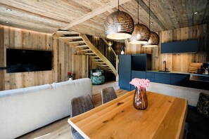 A modern interior with a wooden ceiling, a staircase, a dining area with a wooden table, and a kitchen with a blue countertop.