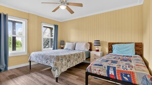 Una camera da letto con due letti, una ventola a soffitto, una finestra con tende e un comodino con una lampada.