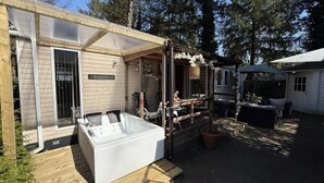 A cabin with a hot tub, outdoor seating, and a covered patio. - Chalet with Jacuzzi and Private Garden - Shared Pool in Summer Season (Hoenderloo)