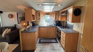 A compact RV kitchen with wooden cabinetry, a gas stove, and a sink. - Chalet with Jacuzzi and Private Garden - Shared Pool in Summer Season (Hoenderloo)