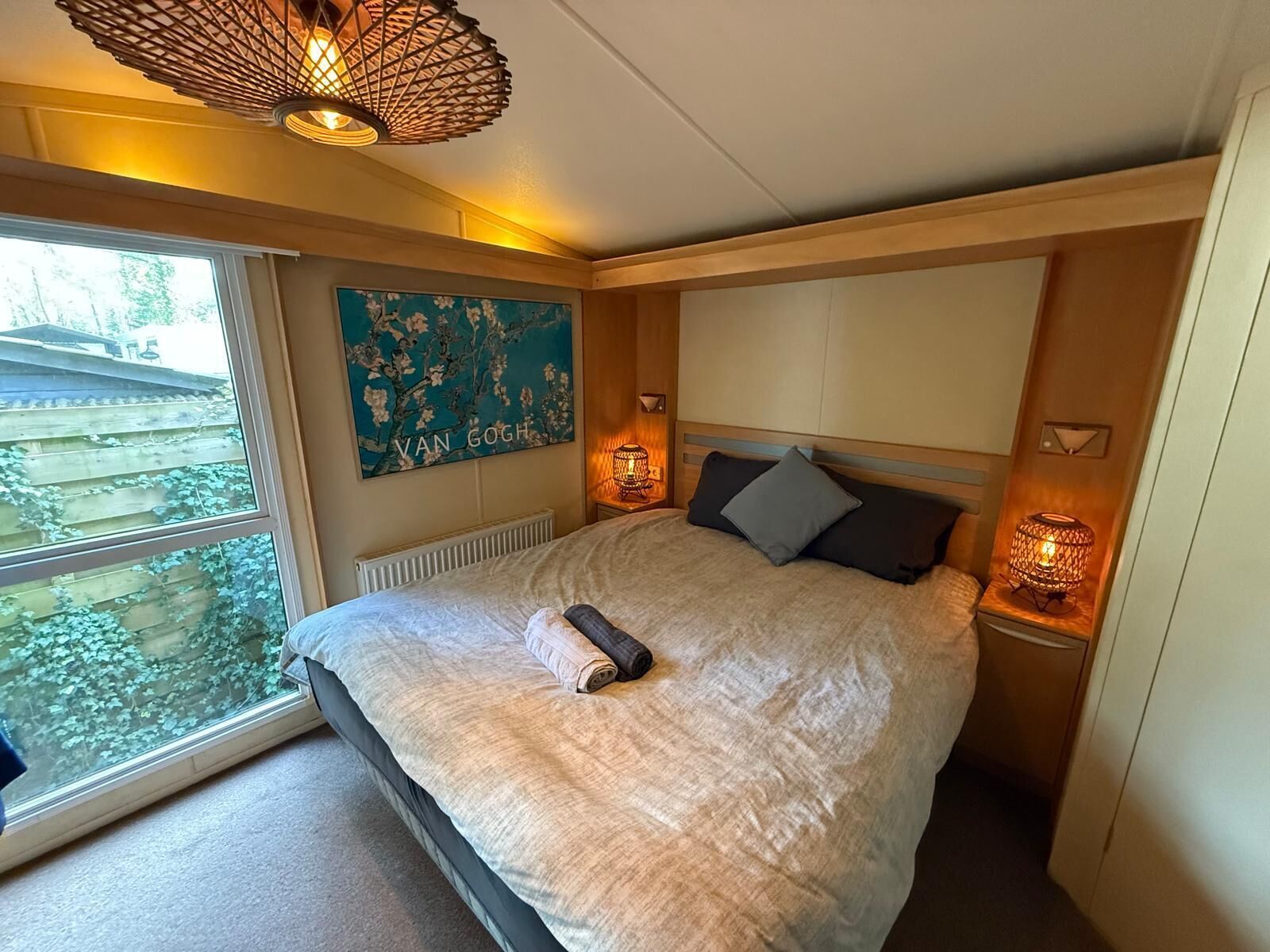 Una camera da letto con un letto grande, una finestra vista verde, un dipinto di Van Gogh e un lampadario originale.