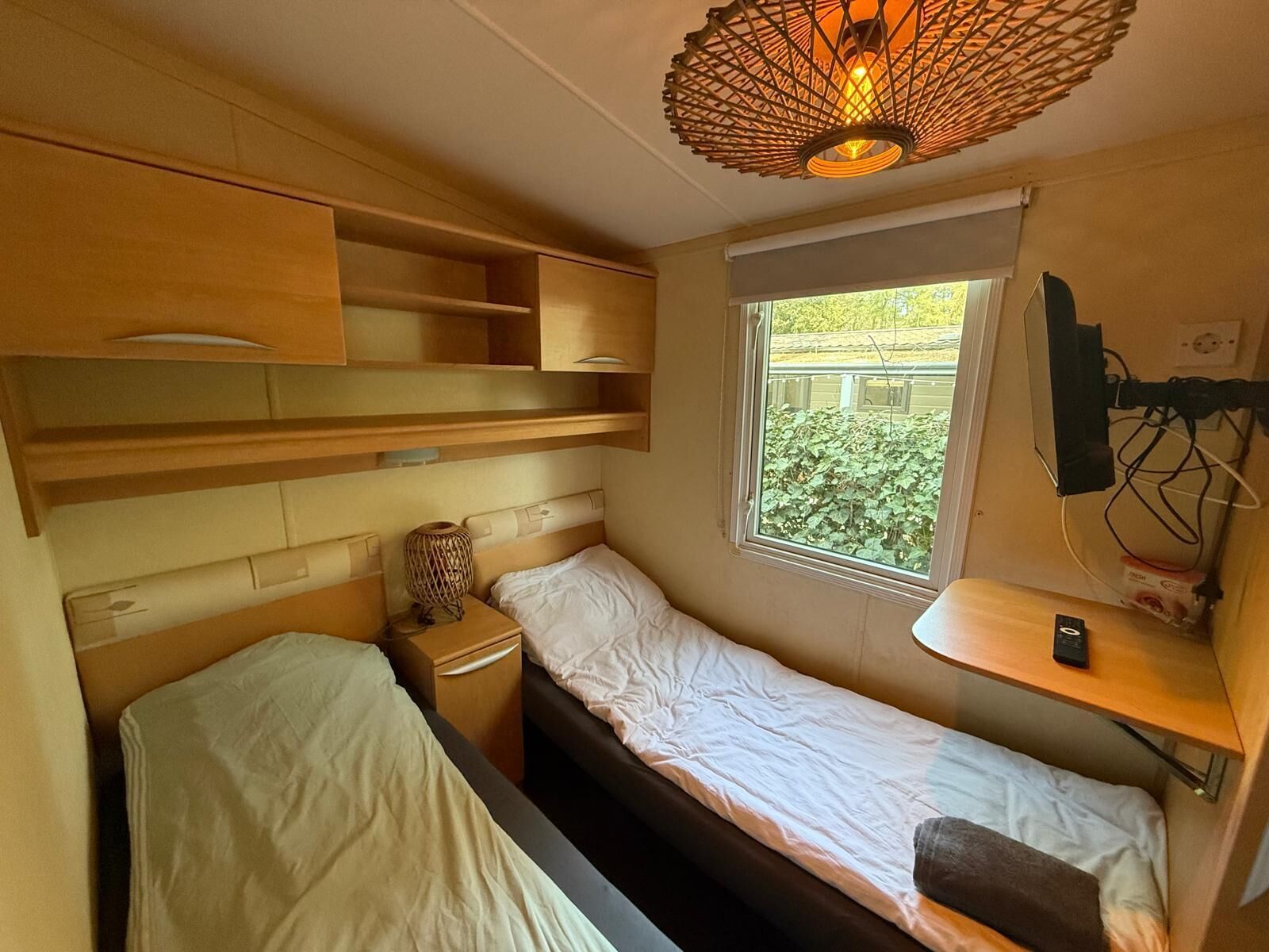Ein kleines Zimmer mit Bett, Nachttisch, Lampe, Fenster mit Blick und einem Regal mit Telefon.