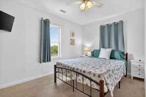 A bedroom with a bed, a nightstand, a lamp, a ceiling fan, and a window with curtains. - UNIT A: Walk to Beach/Intercoastal/Fishing Pier. Drive to Golf/Deep Sea Fishing (Holly Ridge)